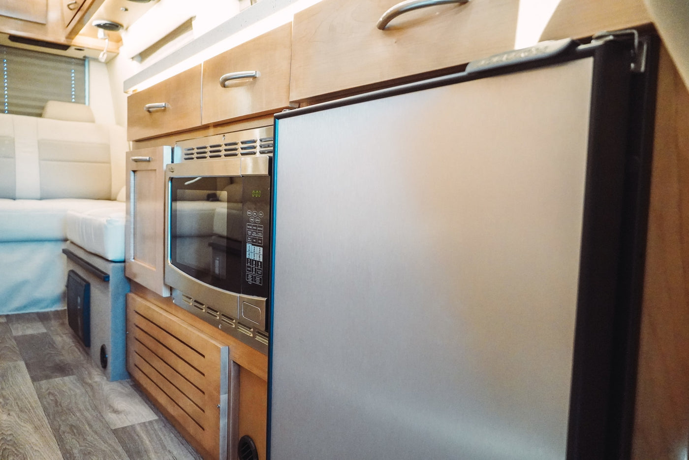 Bright, functional RV rental kitchen with stainless steel microwave, refrigerator, and light wood cabinets. — photo 19