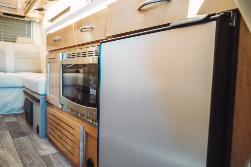 Bright, functional RV rental kitchen with stainless steel microwave, refrigerator, and light wood cabinets. — photo 19