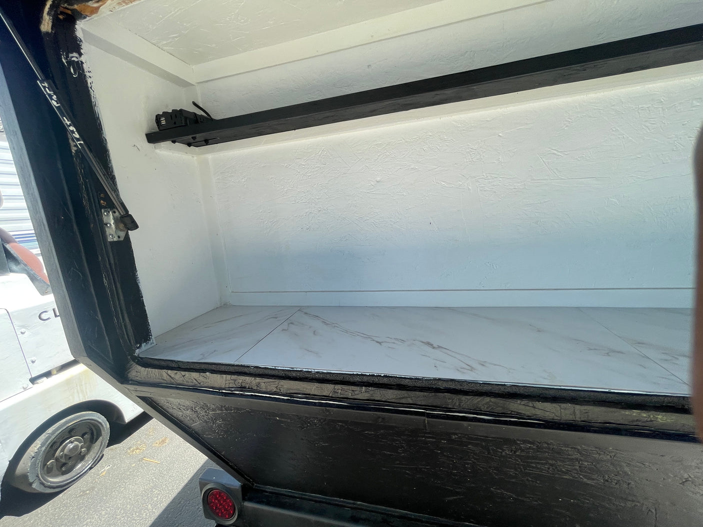 Interior of a compact RV rental, featuring white textured walls, marbled floor, and an overhead power strip.