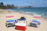Enjoy a Hawaiian beach picnic from your RV rental! Setup includes vibrant chairs, cooler, and camp stove by the ocean.