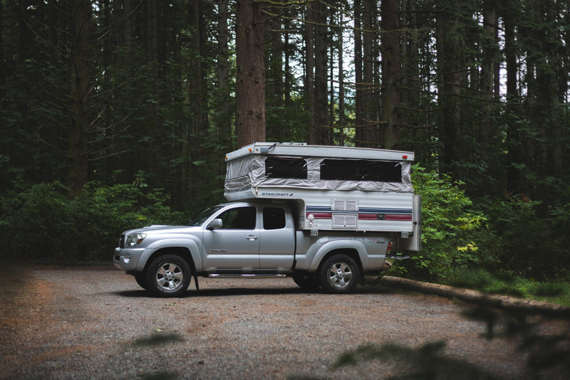 RV rental: A silver Toyota Tacoma with an extended pop-up truck camper, parked on a gravel forest road amidst tall trees. — photo 15