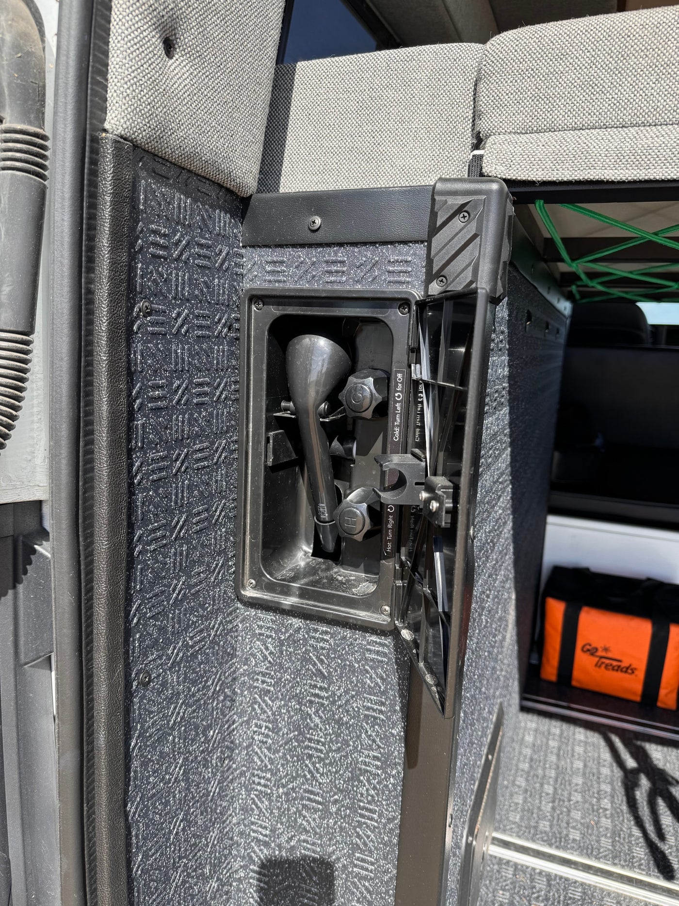 Inside an RV rental, a built-in outdoor shower with hot/cold controls and a textured panel is ready for utility. — photo 16