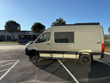 Explore with this tan Mercedes Sprinter adventure van, perfect for RV rental. Parked outside a building on a sunny day.