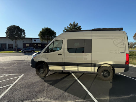 Explore with this tan Mercedes Sprinter adventure van, perfect for RV rental. Parked outside a building on a sunny day.