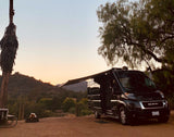 Enjoying a beautiful sunset at a scenic campsite with an extended awning from a black rv rental camper van, ready for adventure.