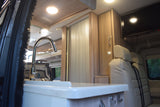 RV rental interior: A bright kitchen with a sink, modern wood cabinetry, and comfortable passenger seating.