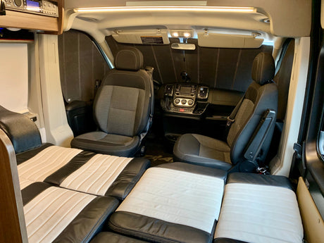 RV rental interior shows swivel driver/passenger seats and a rear bed/lounge area with striped black and white cushions.