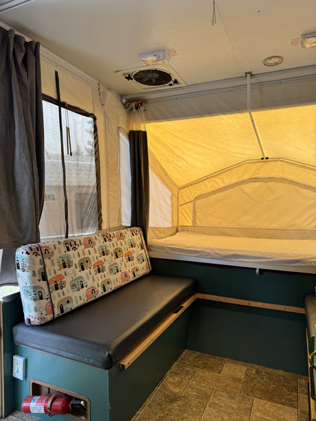 Interior of a comfortable pop-up RV rental, featuring a bench, bed, and essentials for your next camping adventure.