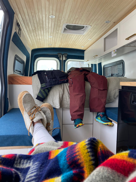 Cozy RV rental interior: feet up with a colorful blanket, winter gear ready, and wooden ceiling.