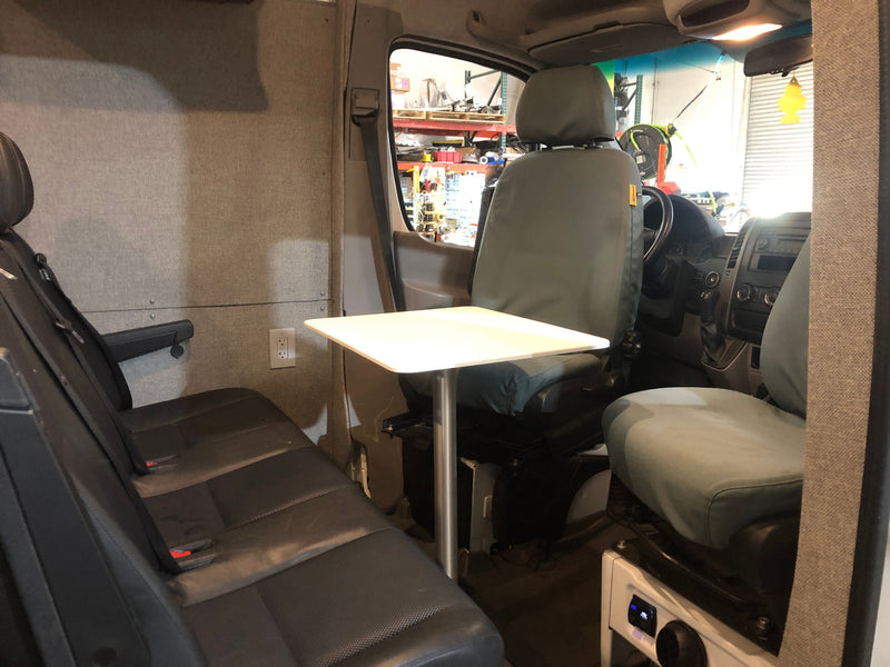 This RV rental interior features rear bench seating, a central table, and an electrical outlet, looking towards the front cabin. — photo 3