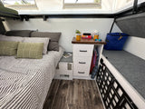 Cozy RV rental bedroom with striped bed, practical nightstand, and smart storage bench for a comfortable travel experience.