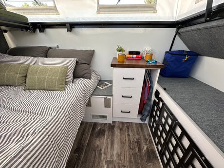 Cozy RV rental bedroom with striped bed, practical nightstand, and smart storage bench for a comfortable travel experience.