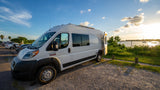 Enjoy scenic views with this rv rental! A white camper van is parked at a waterfront lot under a beautiful sunset sky.