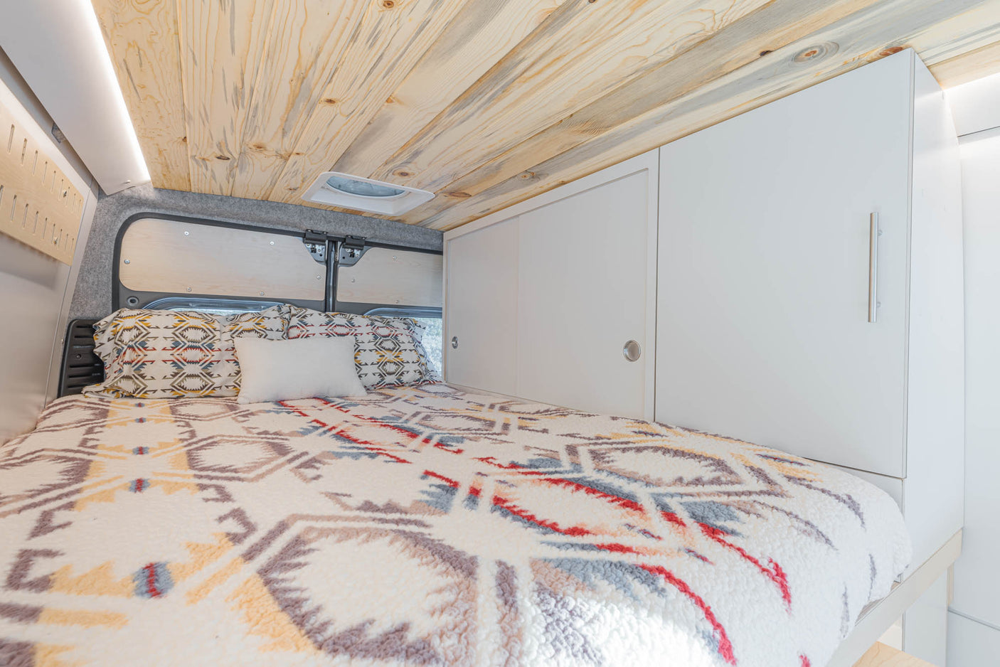 Inviting RV rental bedroom features a cozy bed, natural wood ceiling, white cabinets, and soft LED lighting.
