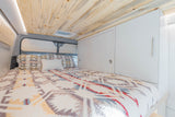 Inviting RV rental bedroom features a cozy bed, natural wood ceiling, white cabinets, and soft LED lighting.
