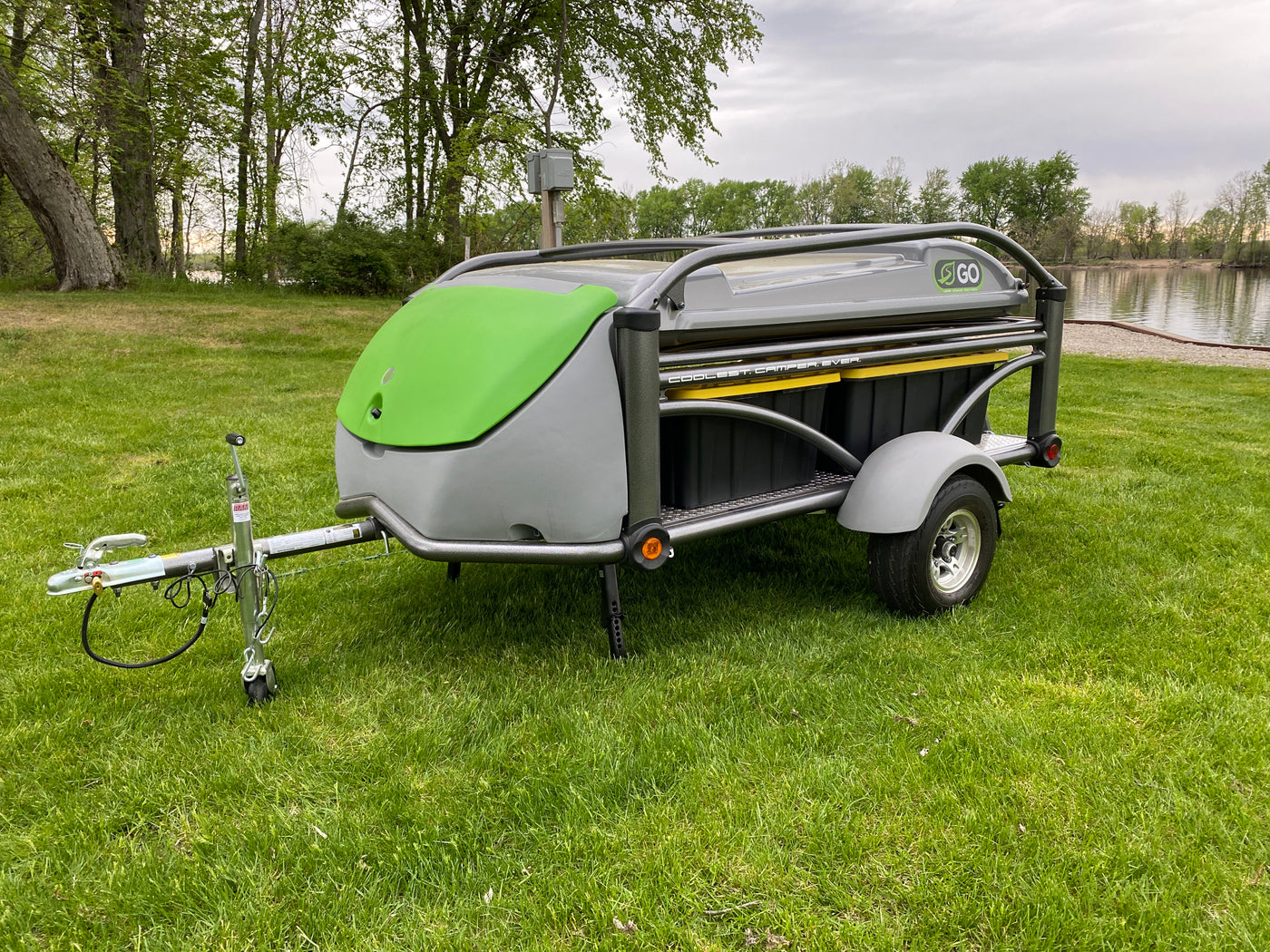 SylvanSport Go compact camper for RV rental, parked on lush grass by a tranquil lake. — photo 2