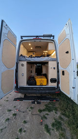 Experience mobile living with this RV rental! Open rear doors of a white camper van, showcasing a cozy bed, storage, and bike rack.