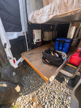 RV rental: Inside a camper van with a bed, Camplux water heater, water tanks, and pull-out storage tray for gear.