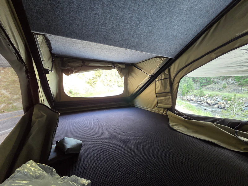 Inside a comfy rv rental rooftop tent, offering scenic river views. Features dark patterned floor, olive walls, and a grey felt ceiling. — photo 9