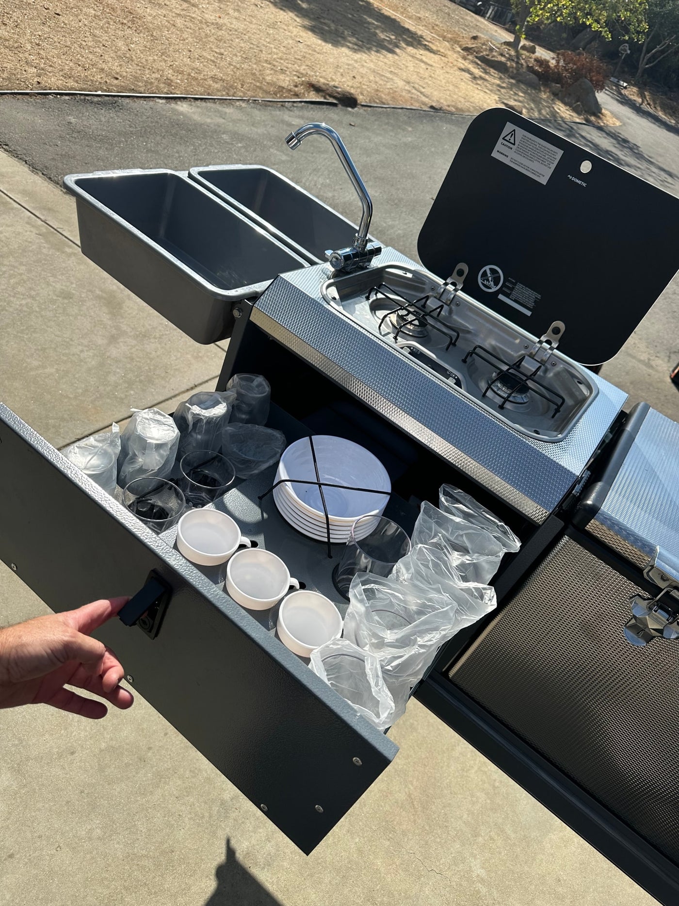 This portable RV rental kitchen features a sink, stove, and organized dinnerware, ready for outdoor cooking. — photo 12