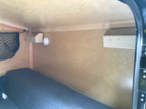Cozy RV rental interior showing a small bed, wooden walls, overhead storage net & bins, and a safety detector.