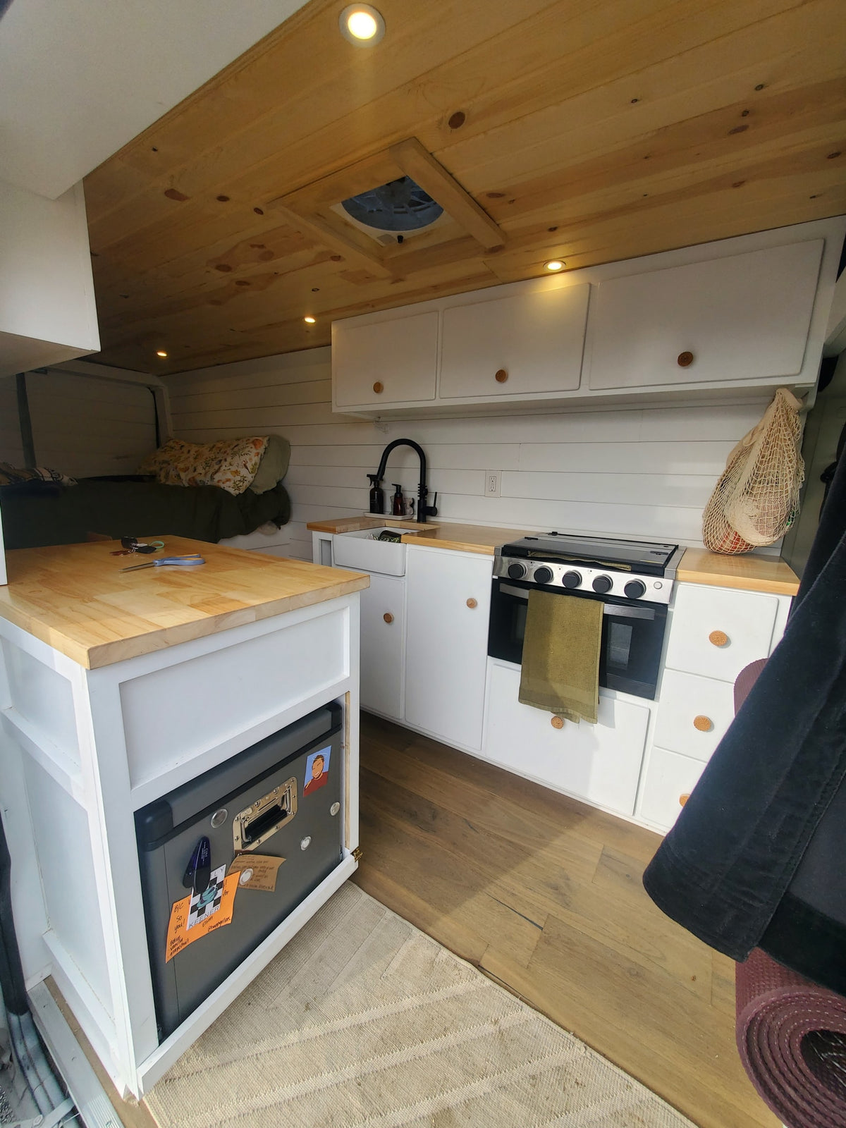  door open to reveal a well-lit bed and interior setup.|Cozy rv rental interior: custom van kitchen with sink — photo 2