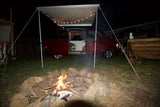 Enjoying an RV rental: a red camper van under a string-lit awning, with a bright campfire in the foreground at night.