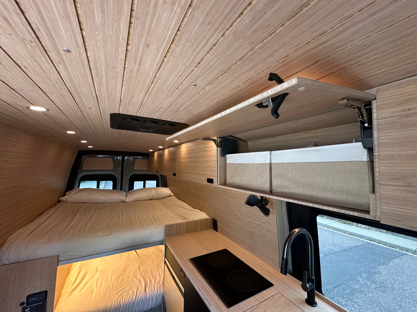 RV rental van interior featuring a cozy bed, compact kitchen, and overhead storage, designed for comfortable travel.