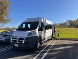 White camper van (rv rental) parked in a lot next to a green field where a toddler stands. Side door open for adventure!