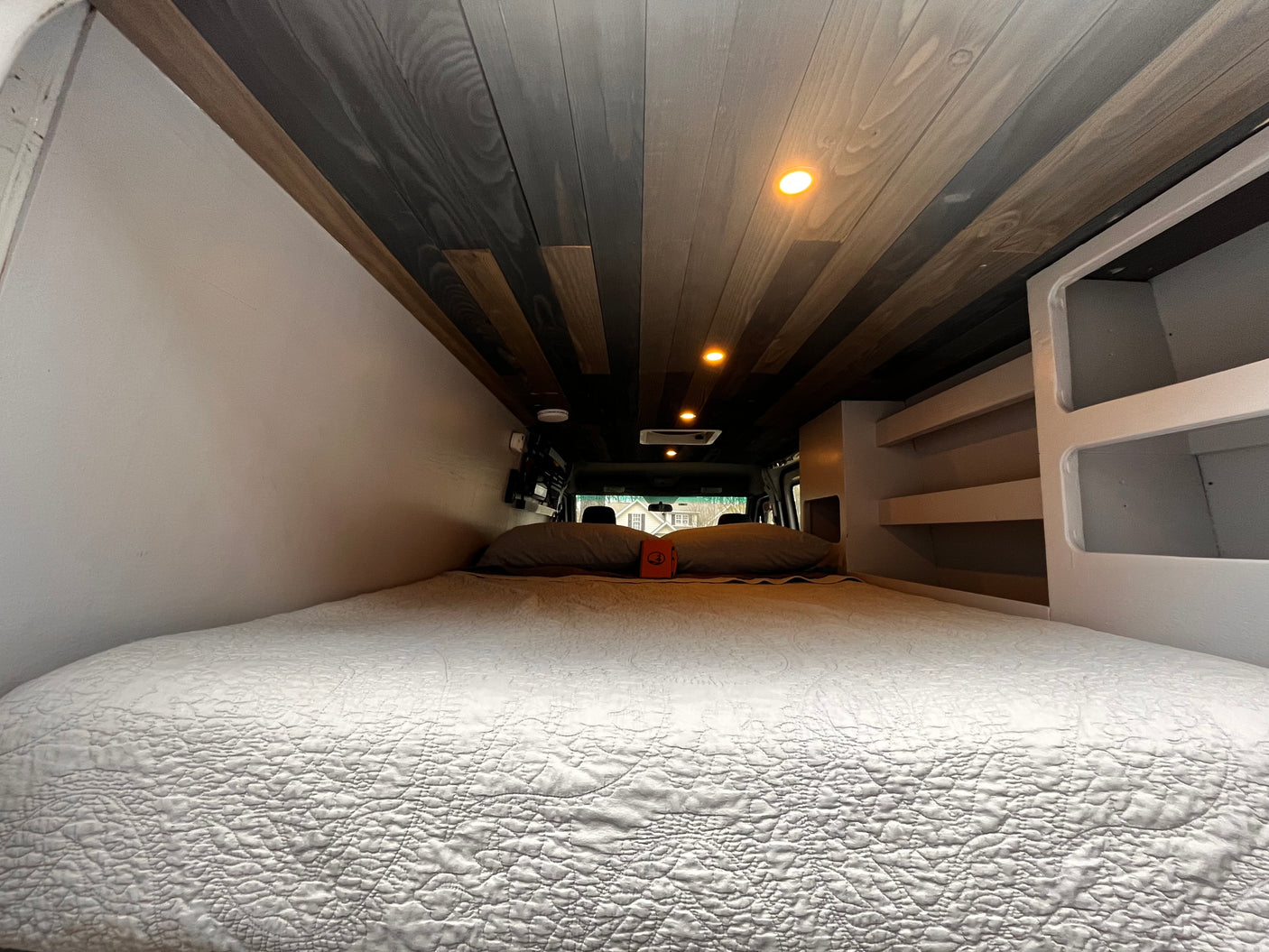 Cozy van conversion RV rental interior with a spacious bed, wood-slat ceiling, and built-in storage. Ideal for mobile living.