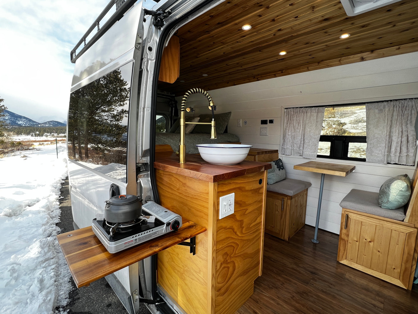 Experience winter adventure in this RV rental! Features a mobile kitchen, extendable stove for outdoor cooking, and cozy custom interior.
