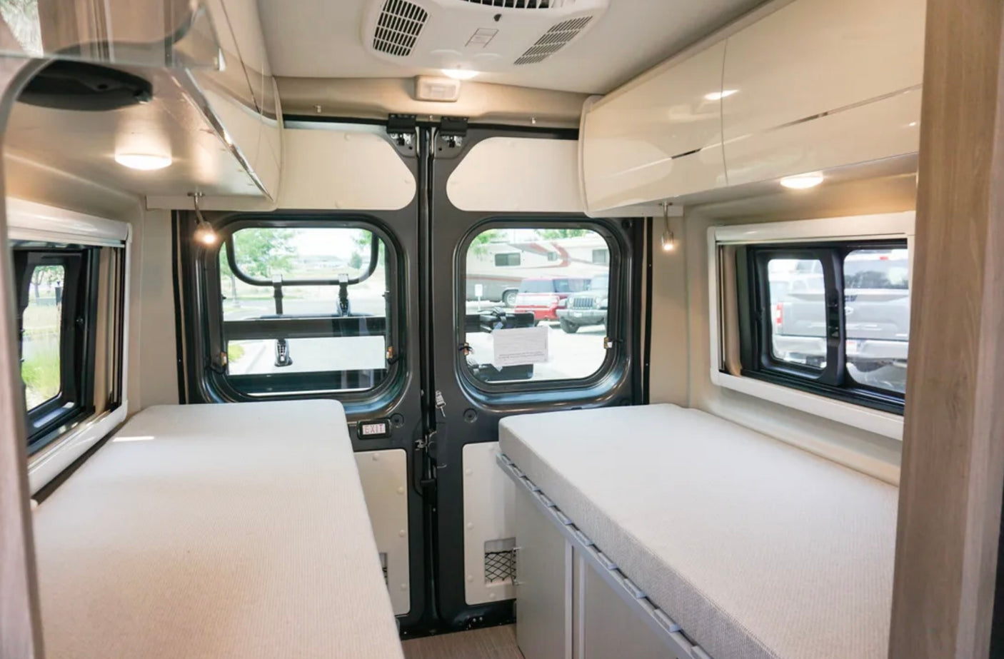 Spacious RV rental interior with dual single beds, overhead storage, and large rear windows for comfort and views.