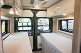 Spacious RV rental interior with dual single beds, overhead storage, and large rear windows for comfort and views.