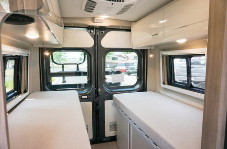 Spacious RV rental interior with dual single beds, overhead storage, and large rear windows for comfort and views.