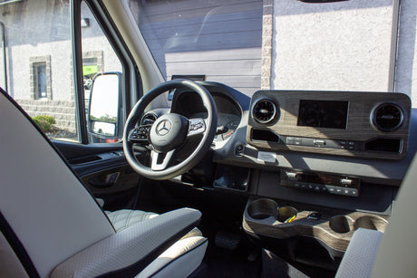 View inside an RV rental: Mercedes-Benz dashboard with wood trim, large screen, and steering wheel.