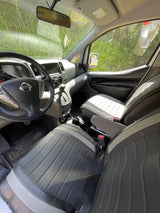 Interior of a Nissan van, perfect for your next RV rental adventure. Shows driver's cockpit, passenger seat, and green foliage outside.
