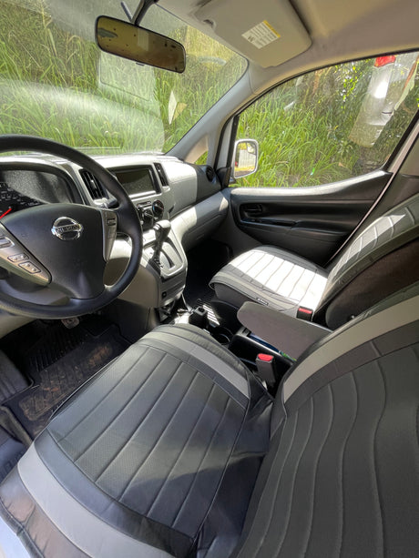 Interior of a Nissan van, perfect for your next RV rental adventure. Shows driver's cockpit, passenger seat, and green foliage outside.