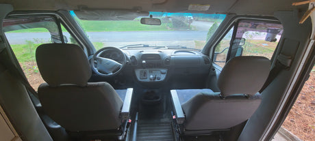 Interior view of an RV rental's cockpit, showing the driver and passenger seats, steering wheel, and dashboard.