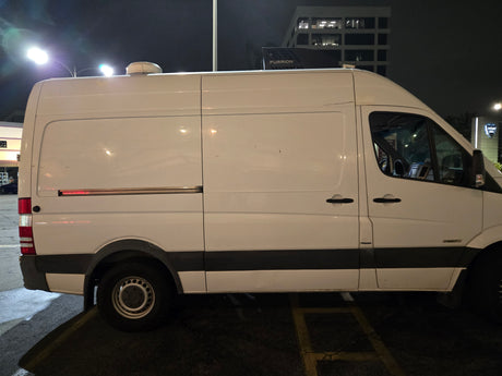 White Mercedes Sprinter camper van, possibly an RV rental, with a Furrion rooftop unit, parked at night.