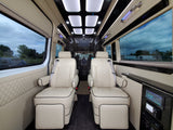 Luxury RV rental interior: two cream, diamond-quilted captain's chairs, modern lighting, sleek tech panel, and dark flooring.