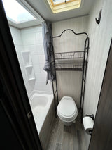 RV rental bathroom: compact design with tub/shower, skylight, toilet, and metal storage shelf. Light walls and wood-look floor.