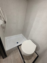 Compact RV rental bathroom featuring a white toilet, shower stall with white base, and light wood-look floor.