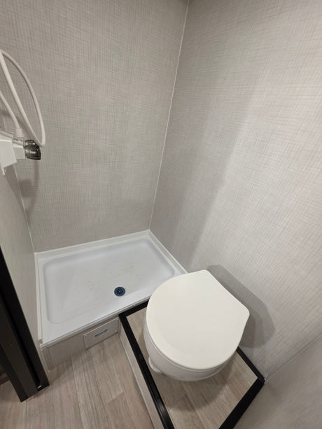 Compact RV rental bathroom featuring a white toilet, shower stall with white base, and light wood-look floor.