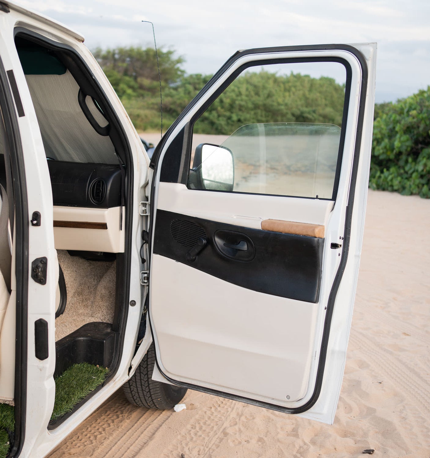 White RV rental van, passenger door open on sand. Interior features a sunshade, dash, and carpet. Perfect for adventure.