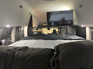 Cozy RV rental camper van interior featuring a large bed and mounted TV for comfortable travel.