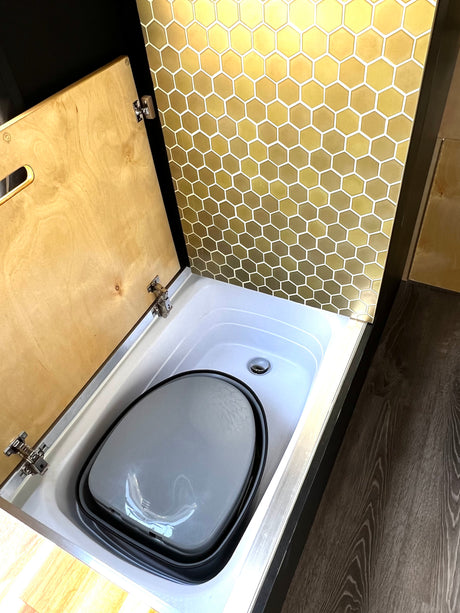 Compact RV rental shower pan/composting toilet with a golden hexagonal tile wall and a hinged wooden cover.