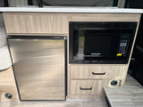 Compact RV rental kitchen with a stainless steel Nova Kool refrigerator, Contoure microwave, and wood-grain cabinetry.