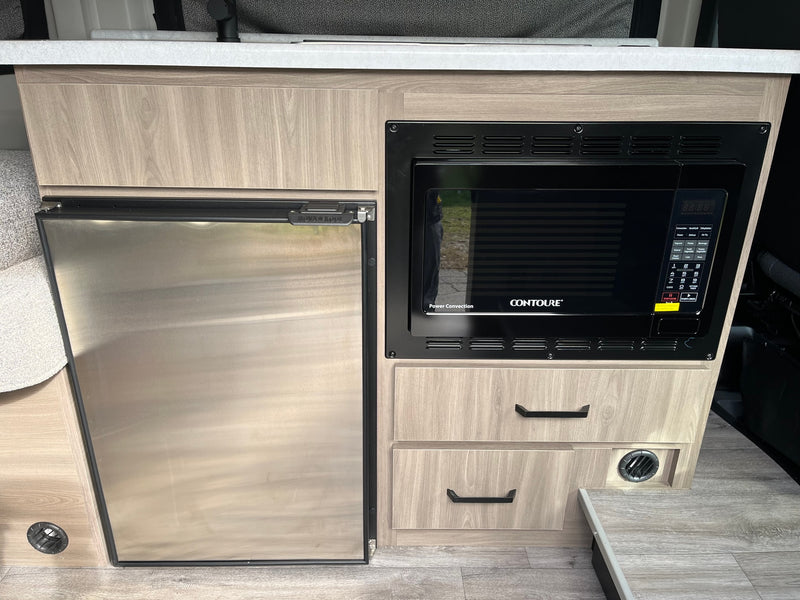 Compact RV rental kitchen with a stainless steel Nova Kool refrigerator, Contoure microwave, and wood-grain cabinetry. — photo 14