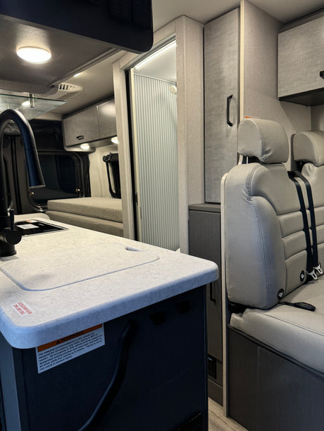 Inside a modern RV rental: a compact kitchen, comfortable seating, and a rear bed area designed for travel.