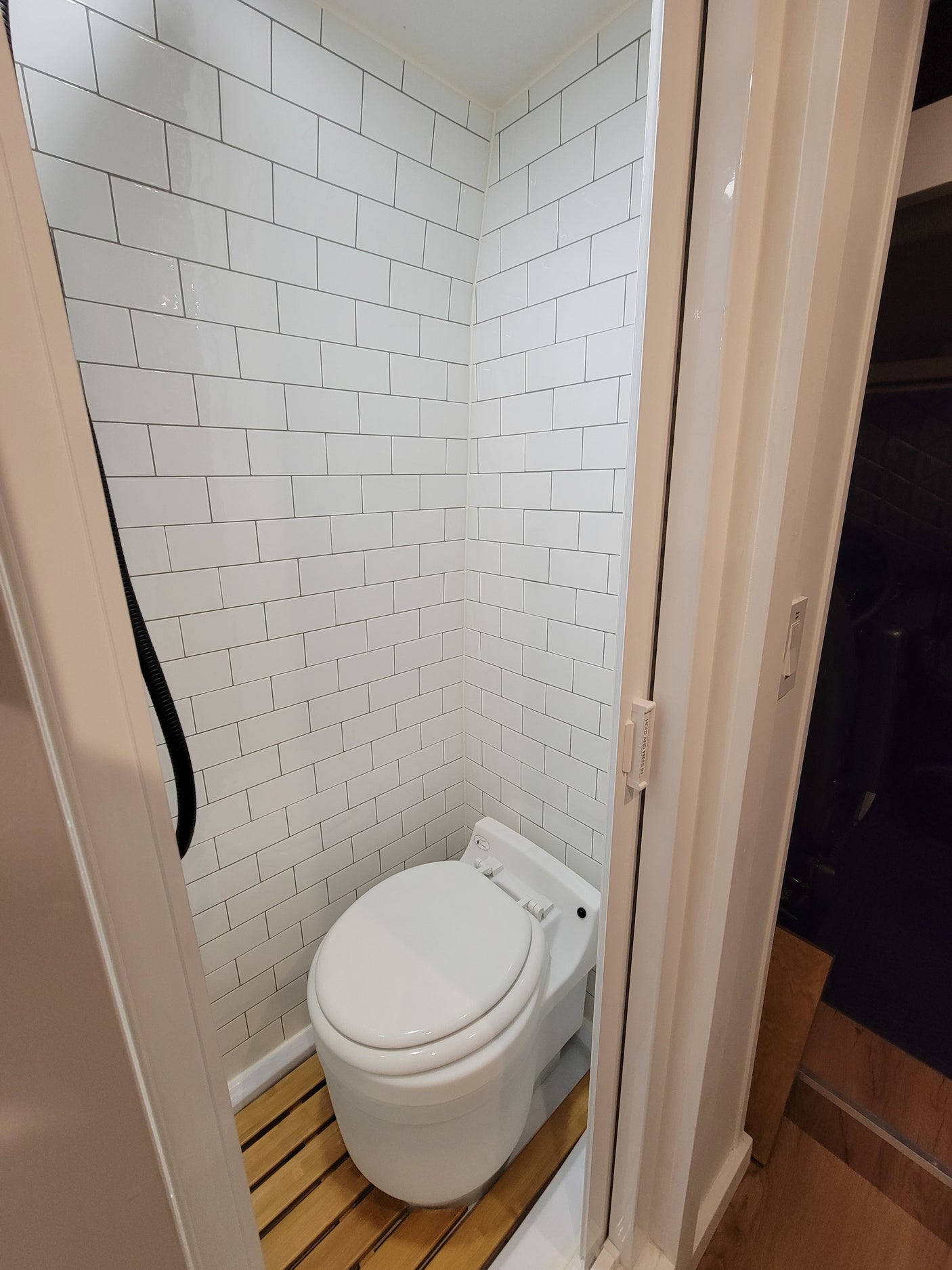 RV rental wet bath featuring white subway tile walls, a white toilet, and a slatted wood shower floor. Functional and compact design.